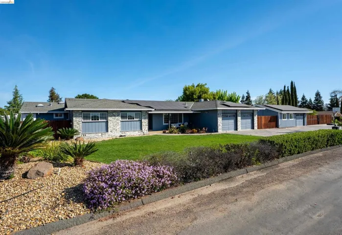 Ranch-style home featuring an attached garage, stone siding, roof mounted solar panels, driveway, and board and batten siding