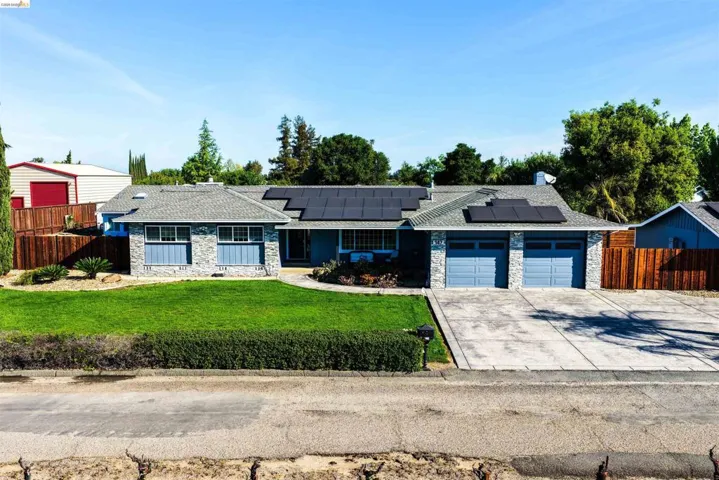 View of front facade featuring stone siding, roof mounted solar panels, concrete driveway, and an attached garage