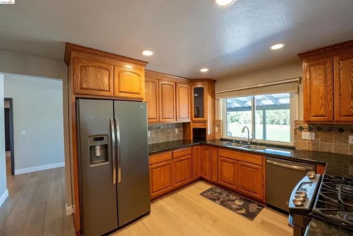 Kitchen with stainless steel appliances, wood finish cabinetry, light wood-type flooring, recessed lighting, and glass insert cabinets