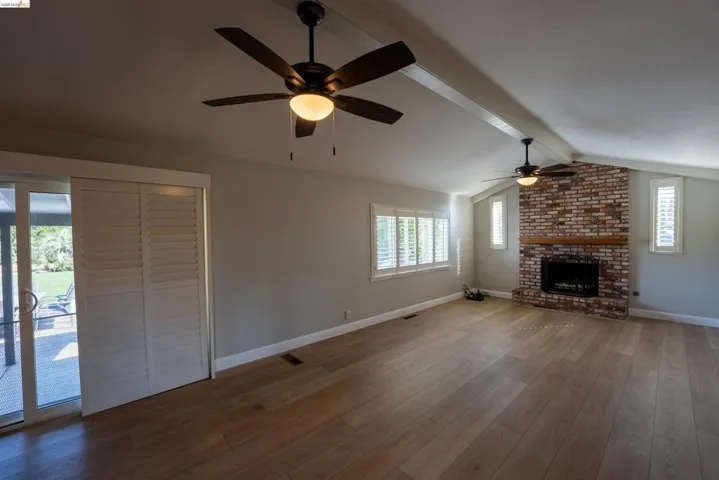 Unfurnished living room with beamed ceiling, a brick fireplace, dark wood finished floors, and a ceiling fan