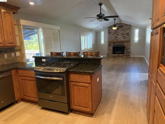 Kitchen with wood finish cabinets, stainless steel appliances, dark stone countertops, light wood finished floors, and beamed ceiling