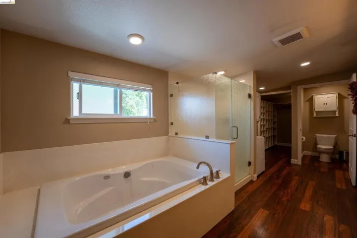 Full bath with a walk in closet, a bath, a stall shower, and dark wood-style flooring