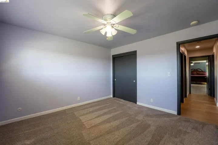 Unfurnished bedroom with dark carpet, a closet, and a ceiling fan