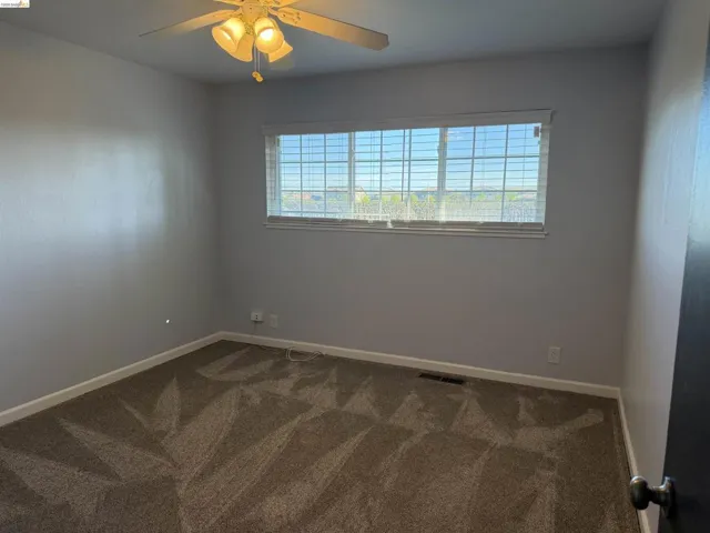 Empty room with a ceiling fan and dark colored carpet