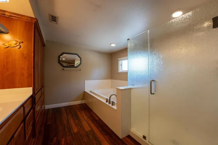 Bathroom with a stall shower, a garden tub, vanity, dark wood-style floors, and recessed lighting