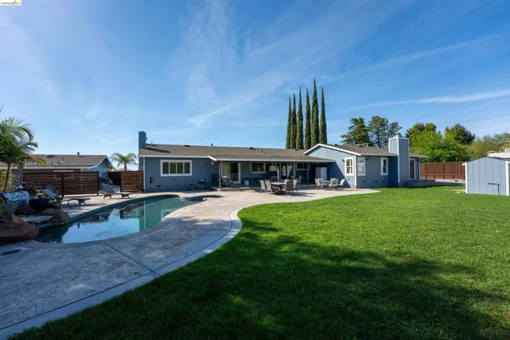 Rear view of house featuring a patio area, a fenced backyard, board and batten siding, and a shed