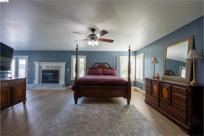 Bedroom with a textured ceiling, light wood finished floors, multiple windows, and a ceiling fan