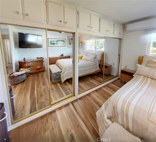 Primary bedroom featuring wall-to-wall mirrored closets with overhead cabinetry offering exceptional storage, along with a mini-split system, motorized shades, modern ceiling fan, and luxury vinyl flooring.