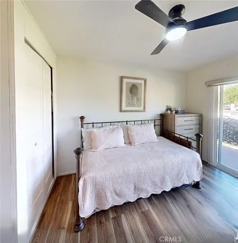 Light-filled guest bedroom with wide-plank flooring, a modern ceiling fan, and a functional closet for added storage.