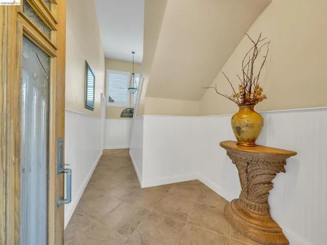 Hallway with a wainscoted wall and lofted ceiling