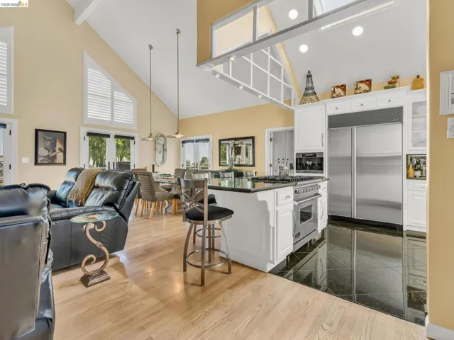 Kitchen featuring open floor plan, premium appliances, white cabinets, a breakfast bar, and lofted ceiling