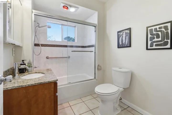 Full bath featuring combined bath / shower with glass door, vanity, and light tile patterned floors