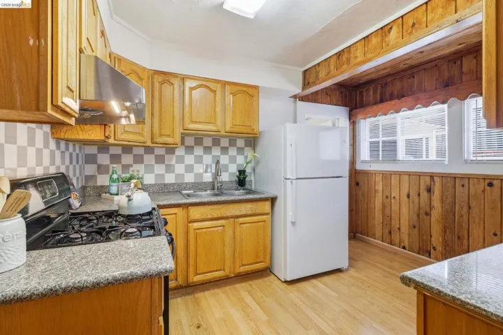Kitchen featuring freestanding refrigerator, range with gas cooktop, wood walls, range hood, and light wood-type flooring