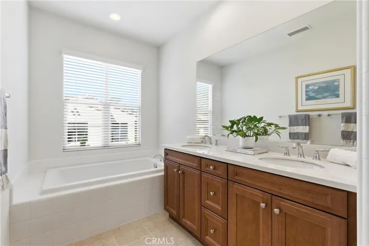 Well-appointed primary bathroom with dual vanities, ample storage, and a soaking tub positioned beneath a large window for natural light.