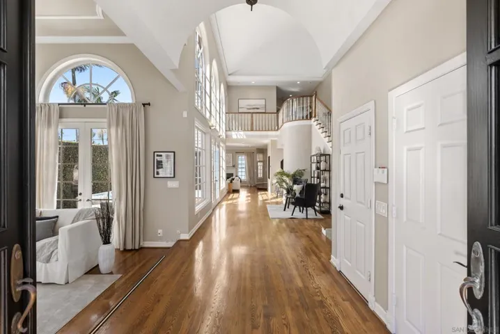 Sunlit volume and soaring ceilings set a graceful tone, where rich hardwood floors, arched windows, and a sweeping staircase create an airy sense of arrival that unfolds with quiet elegance.
