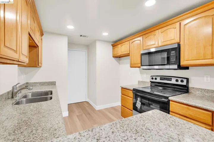 Kitchen featuring black range with electric cooktop, recessed lighting, light wood-style flooring, stainless steel microwave, and light stone counters