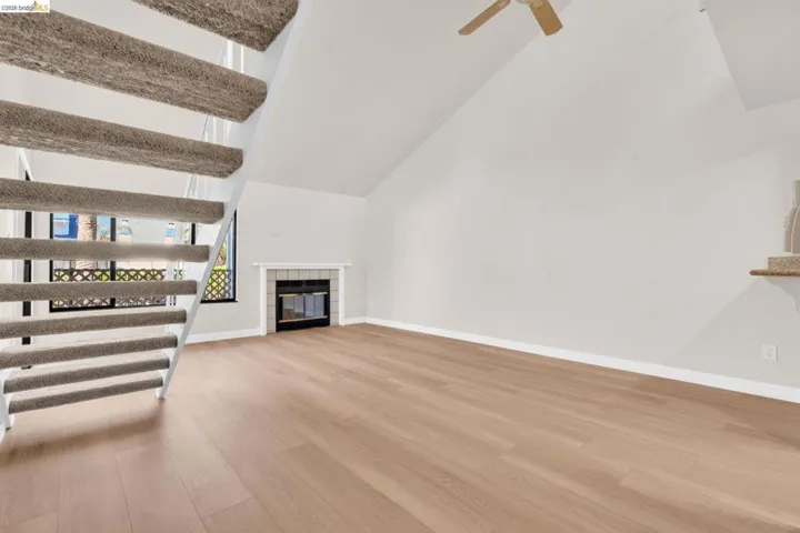 Living room featuring a tiled fireplace, vaulted ceiling, light wood finished floors, and ceiling fan