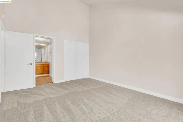 Unfurnished bedroom featuring a high ceiling, light carpet, a closet, and ensuite bathroom