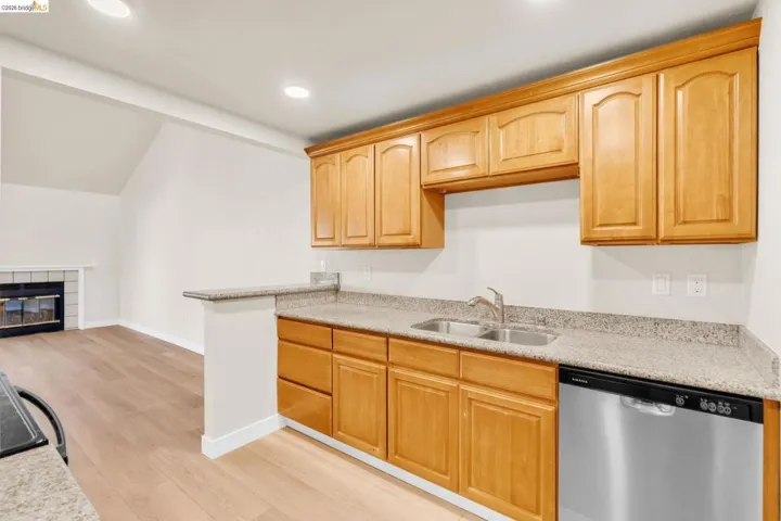 Kitchen featuring dishwasher, light wood-style floors, a fireplace, light wood finish cabinetry, and light stone counters