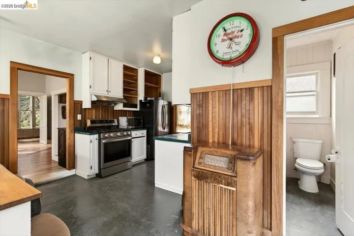Kitchen featuring white cabinetry, stainless steel appliances, dark countertops, wood walls, and open shelves