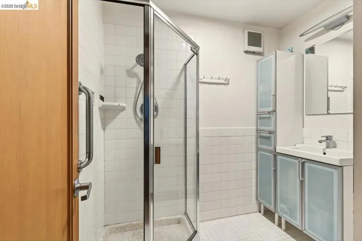 Full bathroom with a shower stall, vanity, tile walls, heating unit, and wainscoting