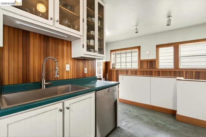 Kitchen featuring white cabinets, wooden walls, glass insert cabinets, wainscoting, and dishwashing machine