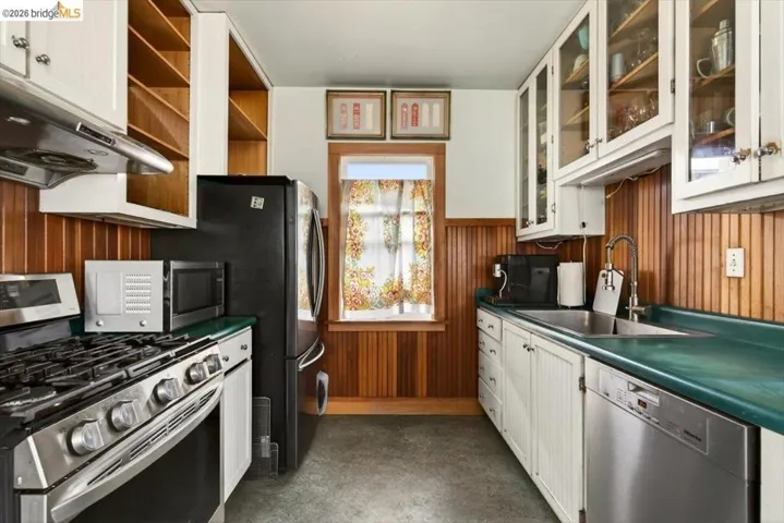 Kitchen with stainless steel appliances, white cabinetry, wooden walls, glass fronted cabinets, and concrete floors