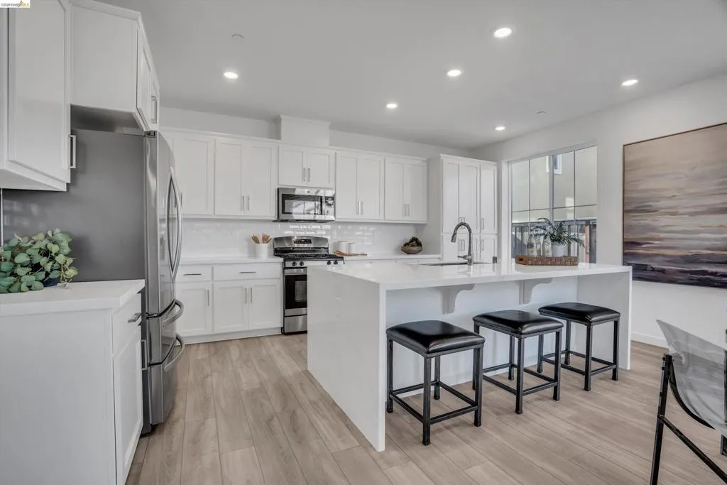 Kitchen featuring a kitchen bar, stainless steel appliances, white cabinets, an island with sink, and recessed lighting