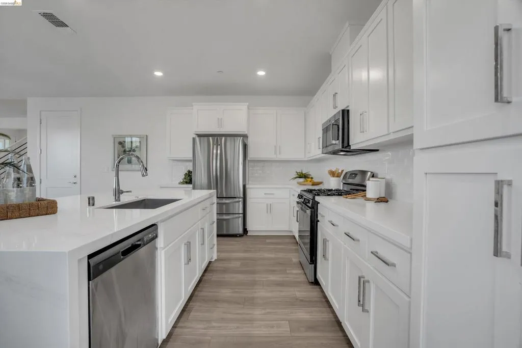 Kitchen with stainless steel appliances, white cabinetry, an island with sink, light stone counters, and recessed lighting