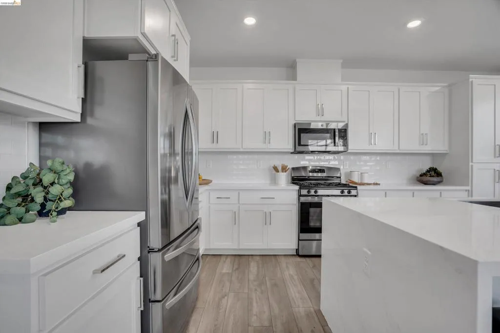 Kitchen featuring stainless steel appliances, white cabinetry, light wood finished floors, light stone counters, and recessed lighting