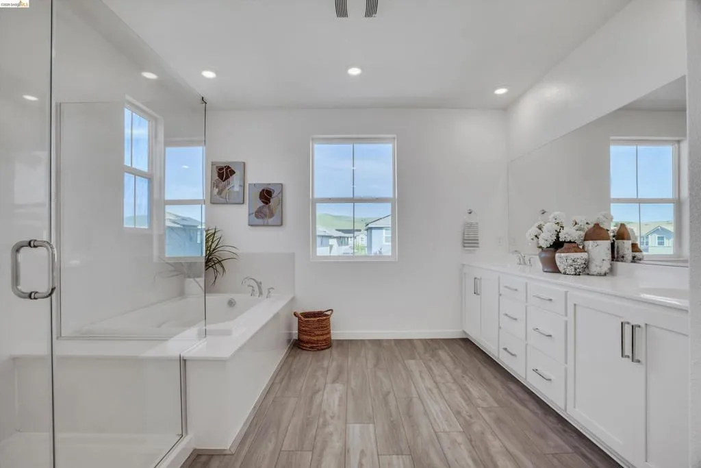 Bathroom featuring a stall shower, light wood-type flooring, double vanity, healthy amount of natural light, and recessed lighting