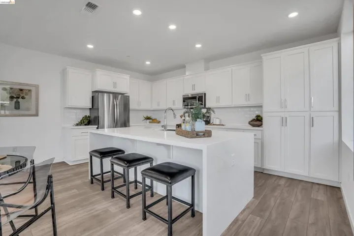 Kitchen with a kitchen breakfast bar, recessed lighting, light wood finished floors, white cabinets, and an island with sink