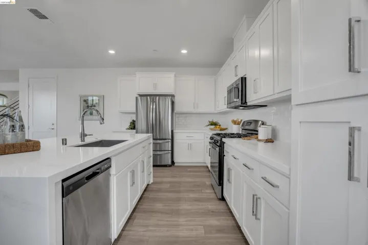 Kitchen with stainless steel appliances, white cabinetry, an island with sink, light stone counters, and recessed lighting