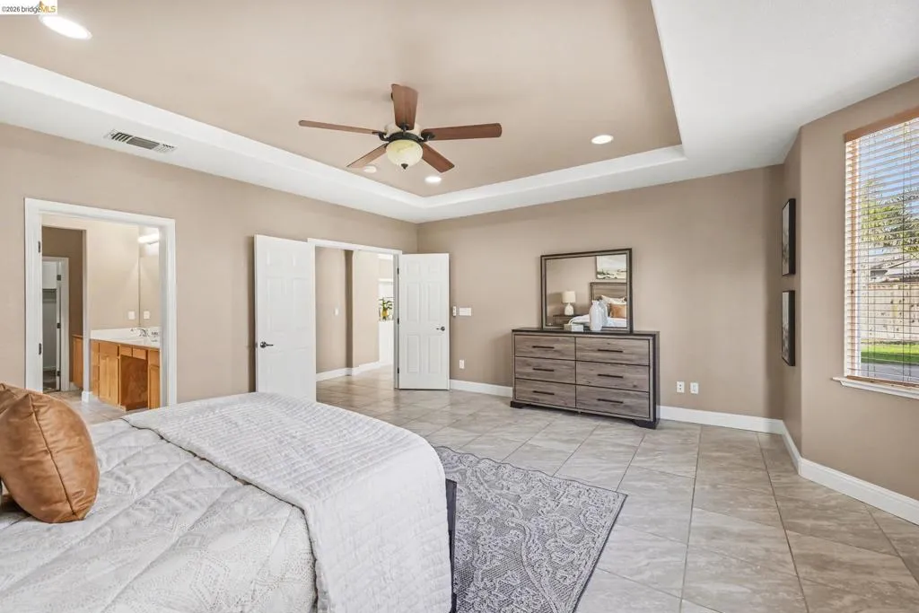 Bedroom featuring recessed lighting, a ceiling fan, ensuite bathroom, a tray ceiling, and light tile patterned floors