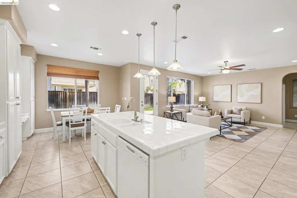 Kitchen with white cabinetry, tile countertops, a center island with sink, dishwasher, and open floor plan