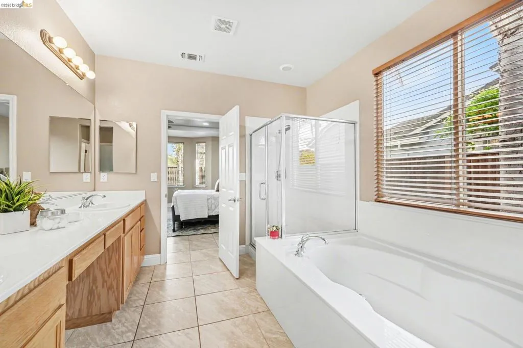 Ensuite bathroom featuring double vanity, a shower stall, a bath, and light tile patterned floors