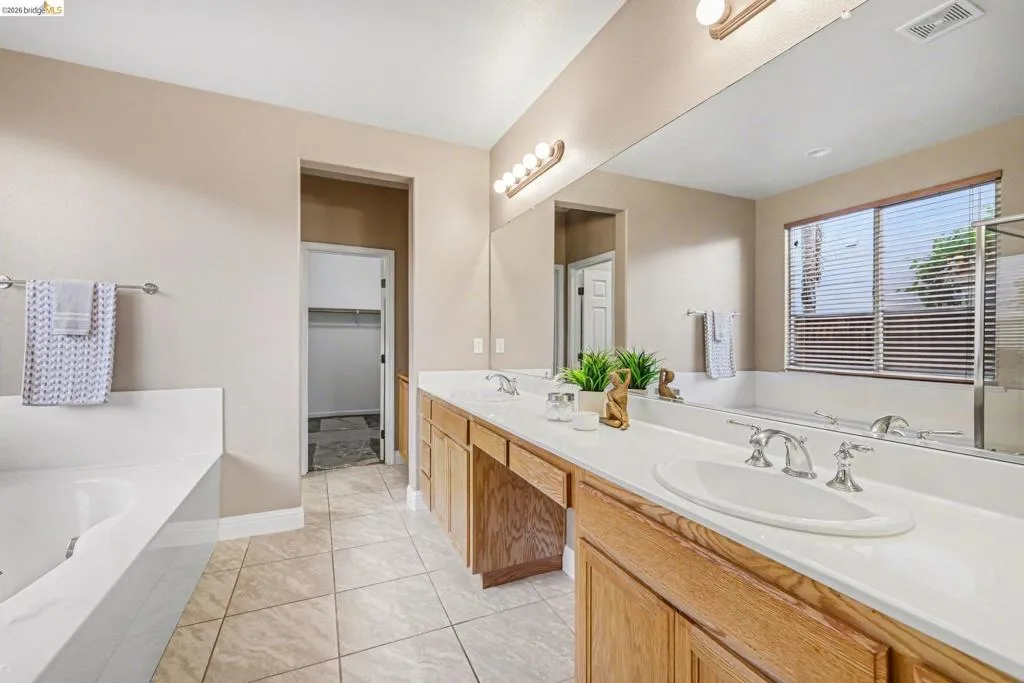 Bathroom featuring a garden tub, double vanity, light tile patterned flooring, and a walk in closet