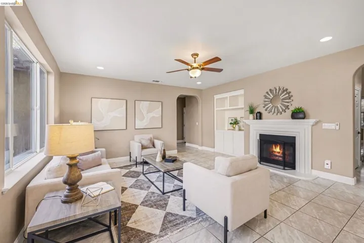 Living area with arched walkways, built in features, ceiling fan, a glass covered fireplace, and recessed lighting