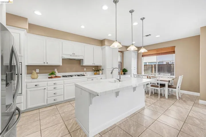 Kitchen with white cabinetry, a kitchen island with sink, stainless steel refrigerator with ice dispenser, and light tile patterned flooring