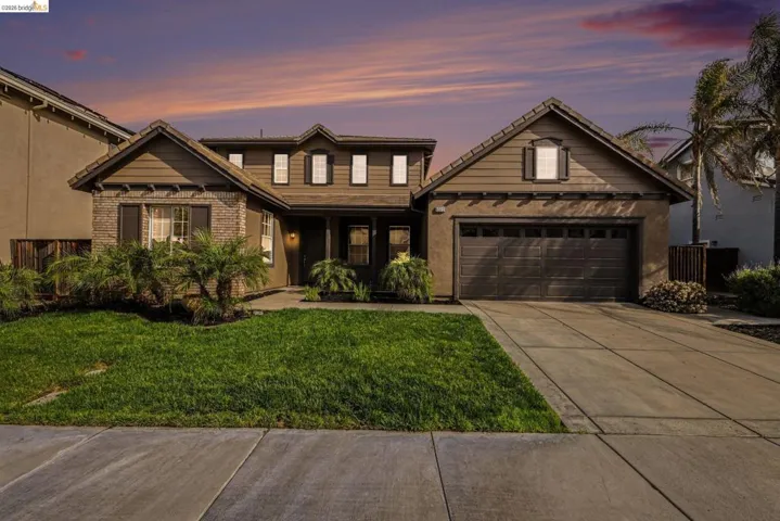 View of front of house with a front lawn, driveway, covered porch, brick siding, and an attached garage