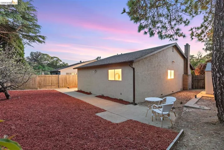 Property exterior at dusk featuring a fenced backyard, a patio, stucco siding, and a shingled roof