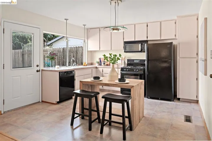 Kitchen featuring light countertops, black appliances, and hanging light fixtures