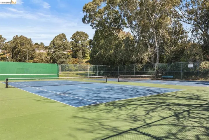 View of tennis court with view of wooded area