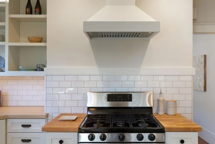 Kitchen with gas stove, exhaust hood, wooden counters, white cabinets, and open shelves