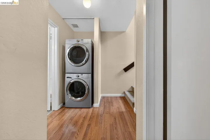 Laundry area featuring a textured wall, light wood-style flooring, and stacked washer and dryer