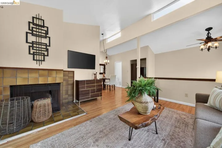 Living room featuring a fireplace, wood finished floors, ceiling fan, a chandelier, and vaulted ceiling