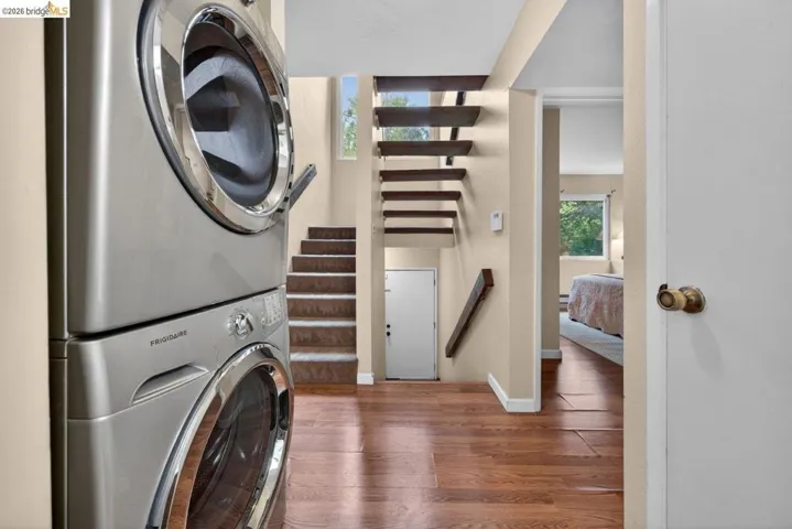 Laundry area featuring dark wood-style flooring and stacked washer / drying machine