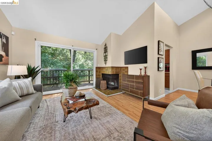 Living room with lofted ceiling, light wood-style flooring, and a fireplace with raised hearth