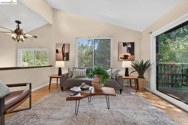 Living room featuring a ceiling fan, light wood-style floors, and lofted ceiling