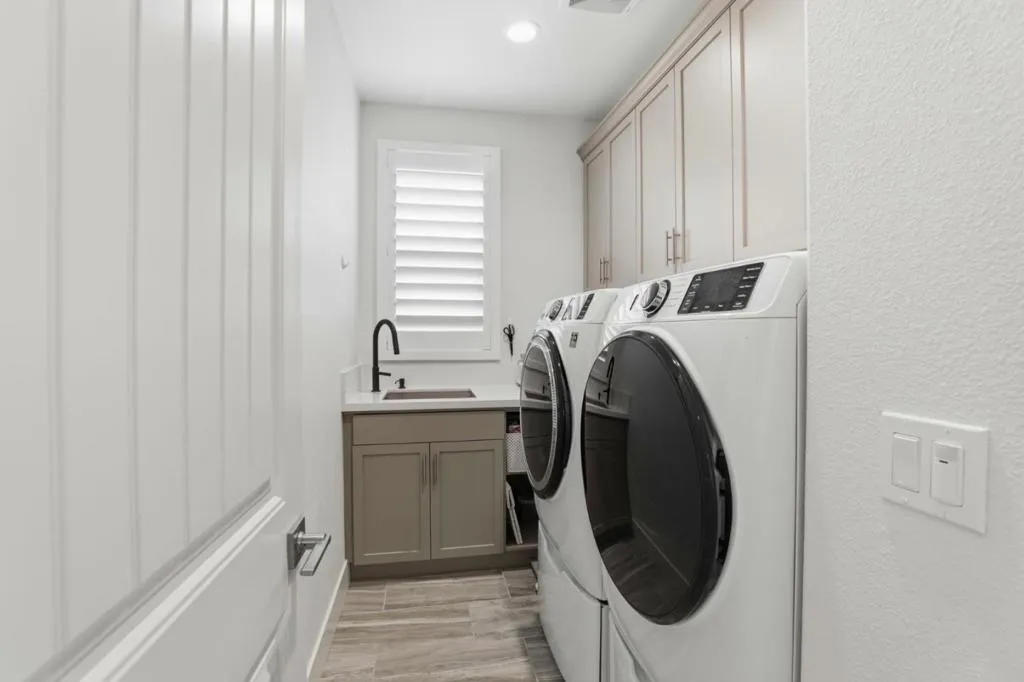 Upstairs laundry room featuring built-in cabinetry, a utility sink, and sleek modern finishes.